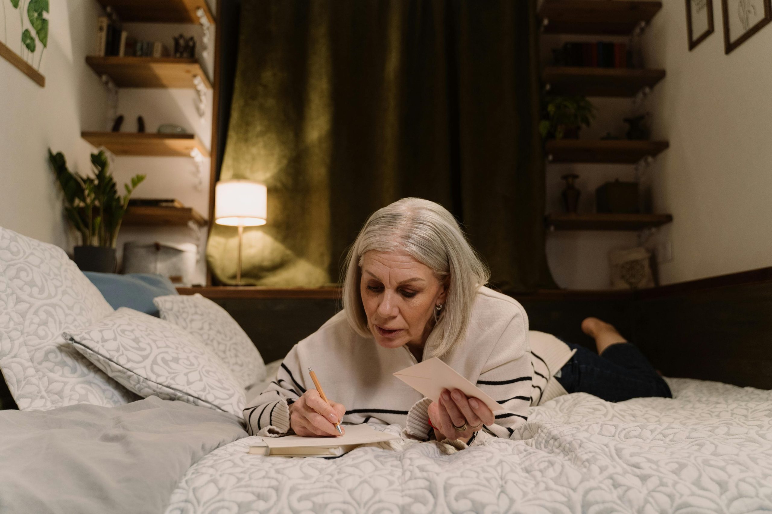 Image shows mature woman lying on bed, appearing to be writing. It illustrates the importance of editing your memoir.